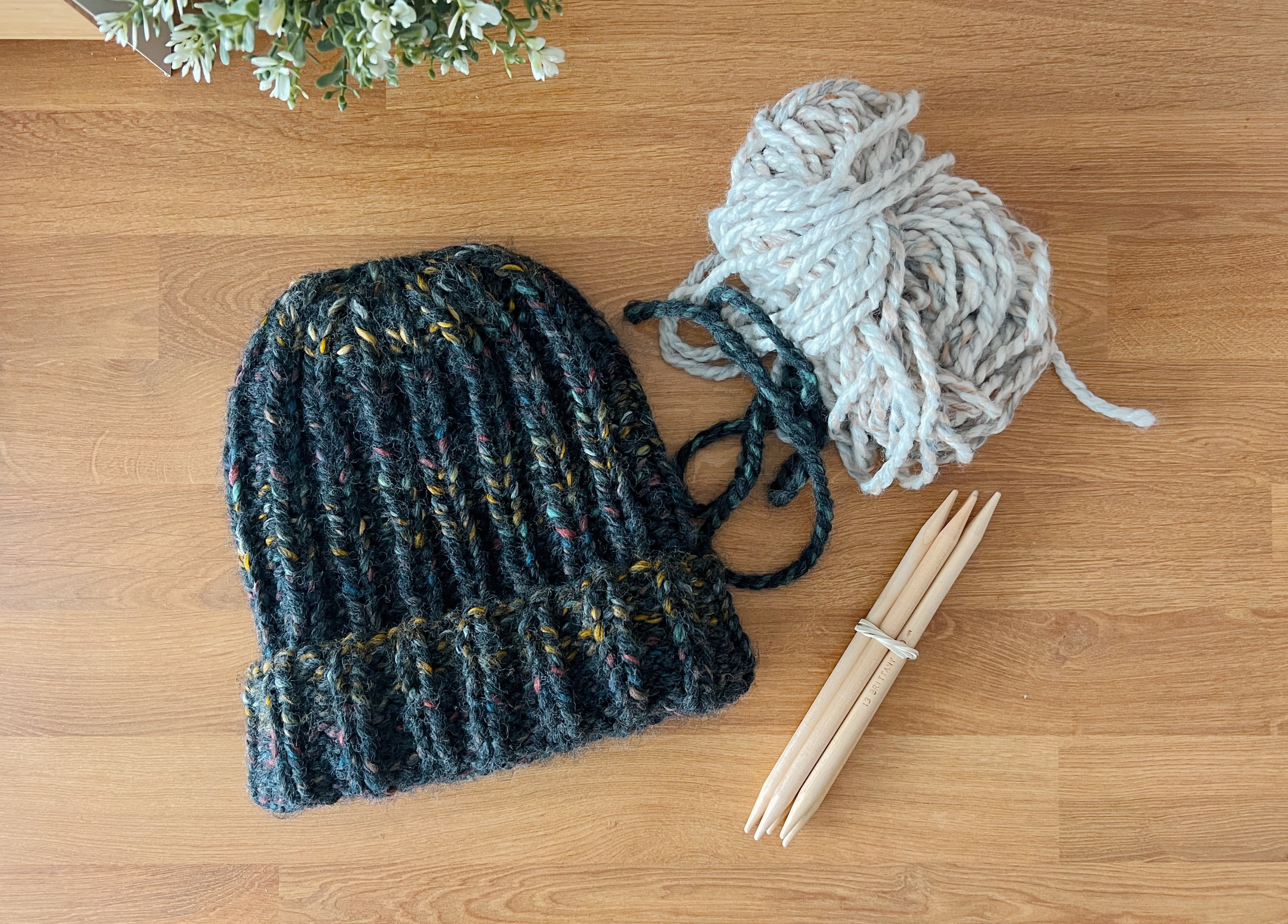 Winter Ale Beanie with yarn and knitting needles on a wooden surface